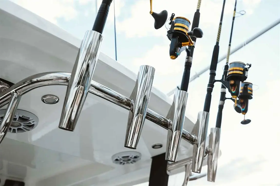 Fishing rods and reels securely stored on a polished stainless steel rack aboard a boat under a bright sky.